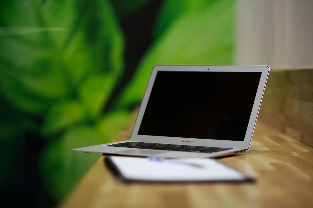 A sleek silver laptop sits open on a wooden desk with a green backdrop, illustrating a modern workspace.