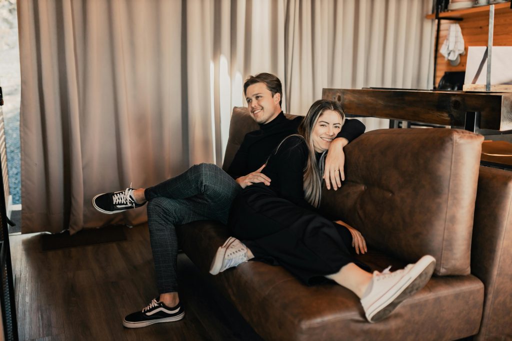 Smiling couple relaxing on a brown leather sofa in a cozy room, enjoying leisure time.