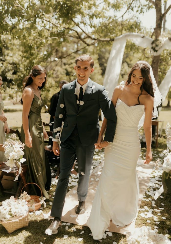 Newlywed couple walking down the aisle outdoors, surrounded by nature and guests.