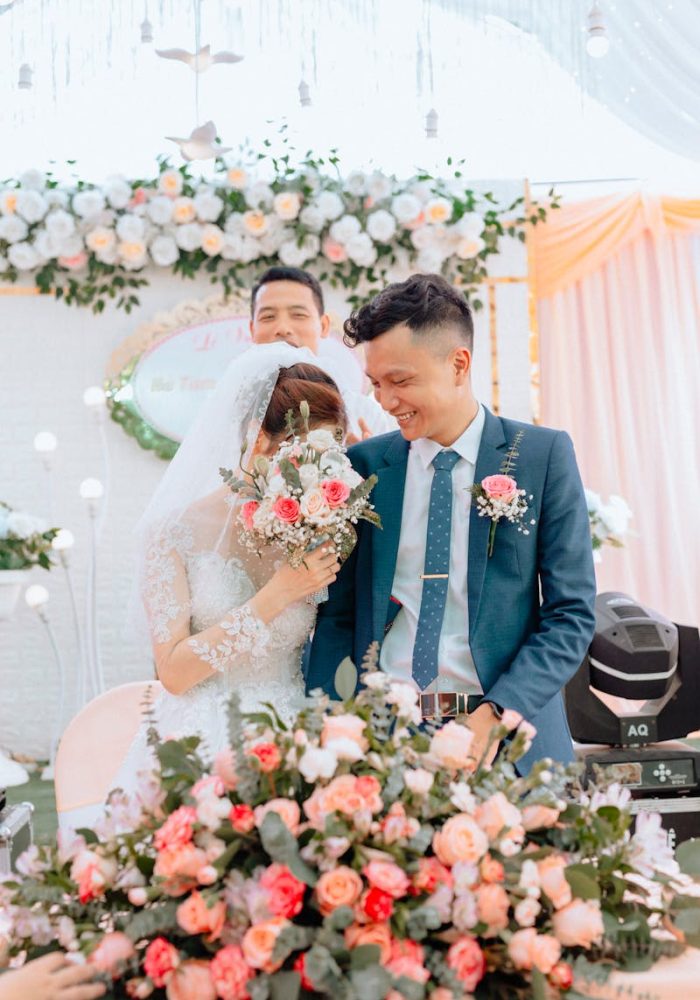 Newlyweds smiling amid lush floral arrangements during a bright wedding ceremony.